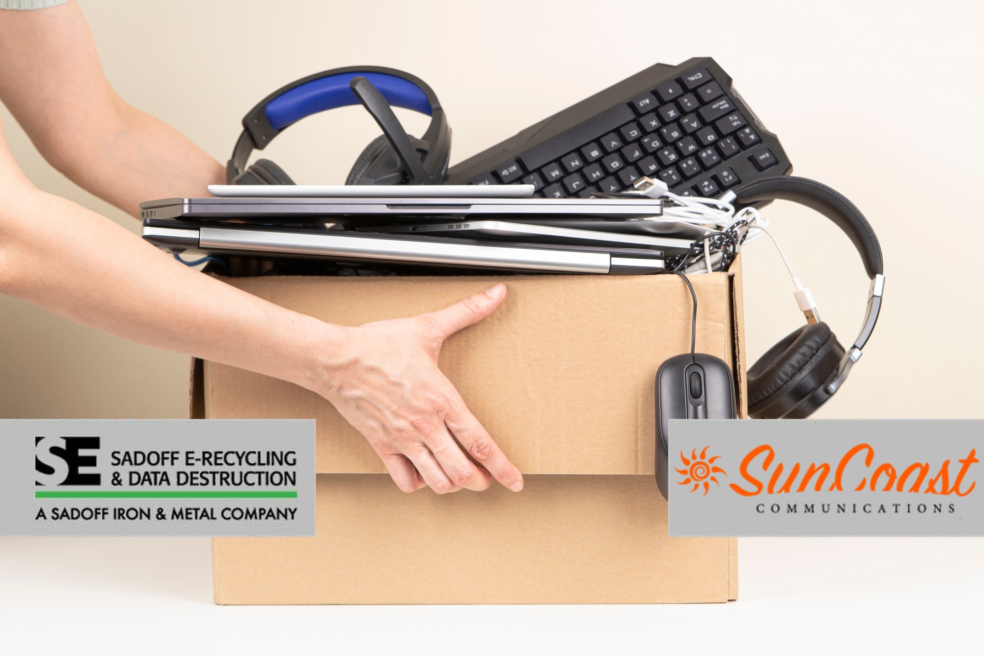 Box of donated laptops, keyboard, and headphones with Sadoff and SunCoast logos